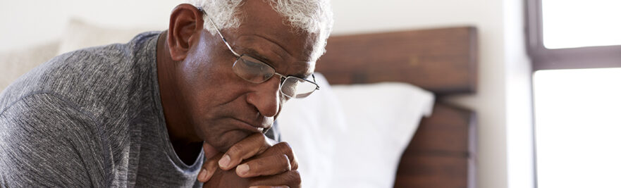 Man sitting on edge of bed looking sad