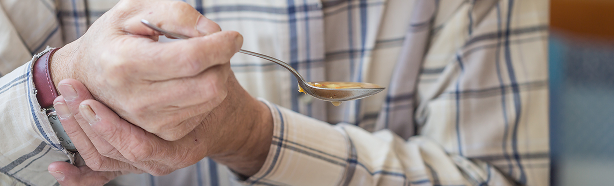Man holding his hand steady while he holds a spoon with soup