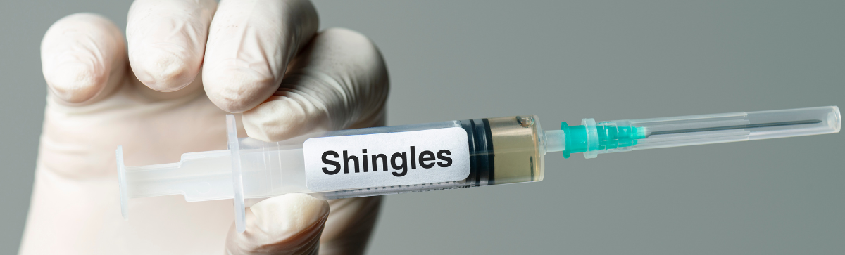 Medical gloved hand holding a syringe that says 'shingles'.