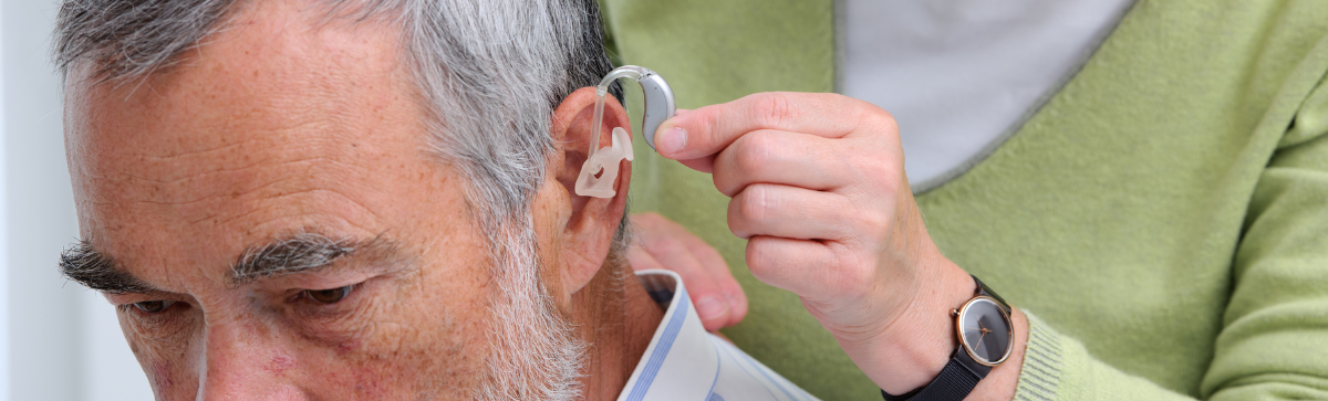 Person assisting in inputting a man's hearing aide.