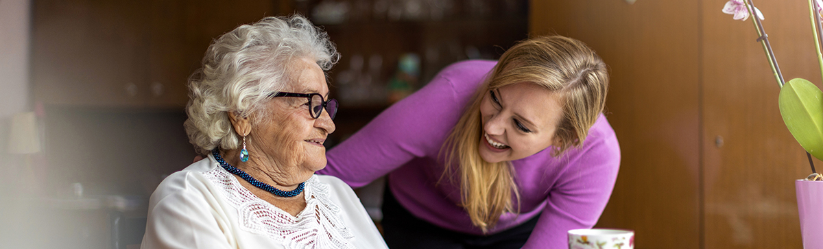 A young woman leans down to smile at an elderly woman